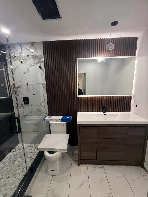 Finished bathroom vanity with illuminated mirror and glass shower enclosure