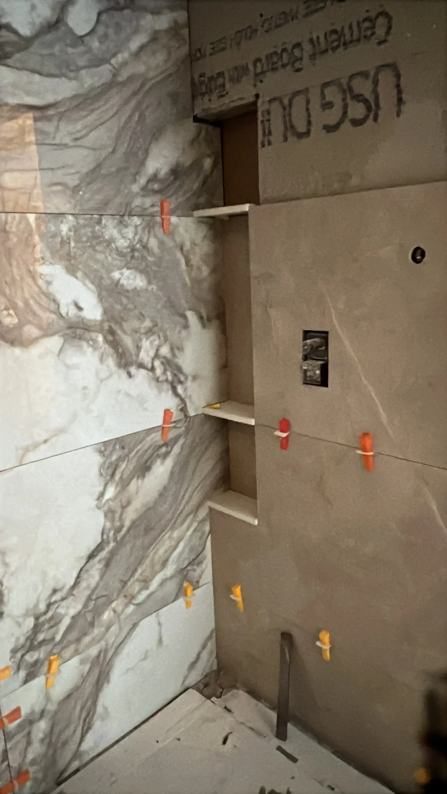 Large wall tiles being installed beside shower backer board