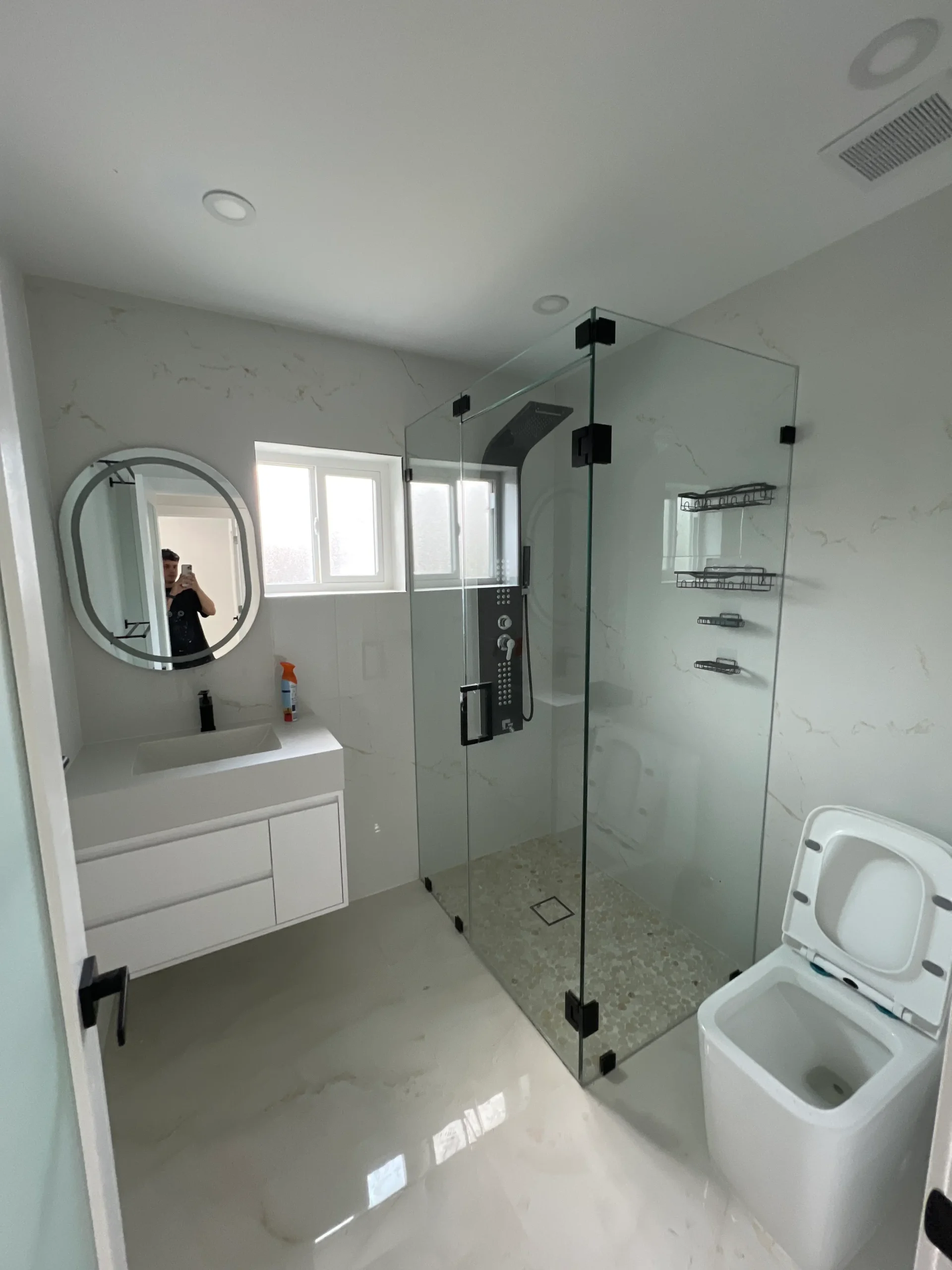 Compact bathroom with glass shower, white vanity and round mirror